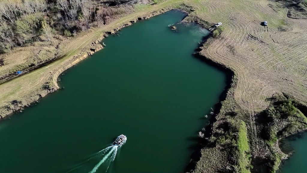 Aerial view of a boat on a green lake, surrounded by grassy banks and trees.