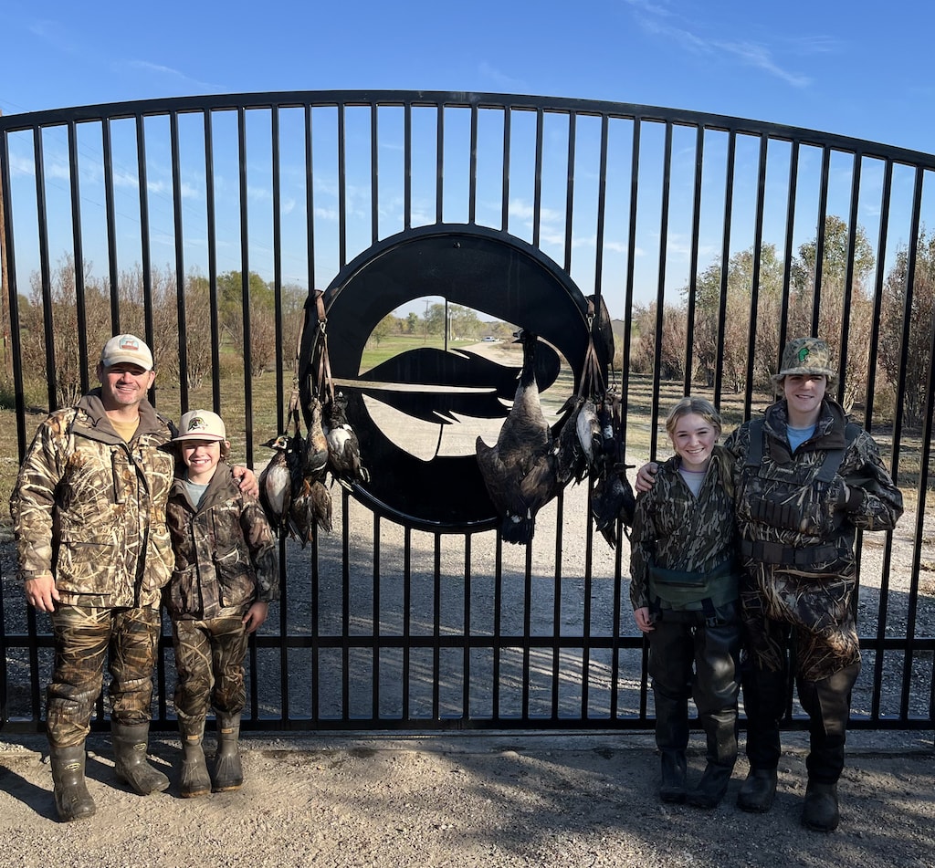 Family duck hunters with their successful hunt, posing at the gate.