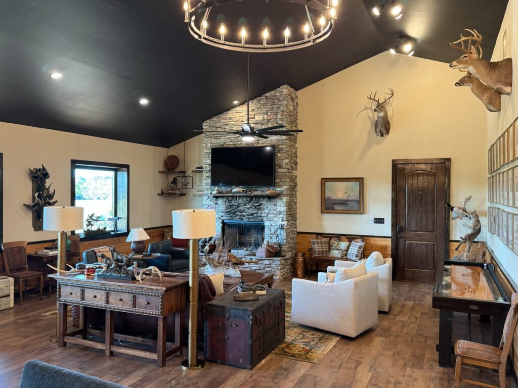 Rustic living room with stone fireplace, antler decor, and cozy seating. Warm lighting and wooden accents create a welcoming atmosphere.
