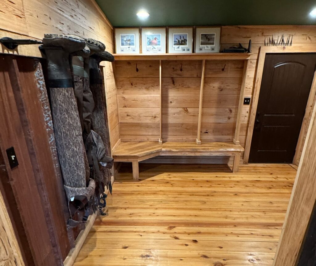Rustic wooden mudroom with benches, boot storage, and coat hooks, featuring framed photos and a wooden door, creating a cozy entry space.