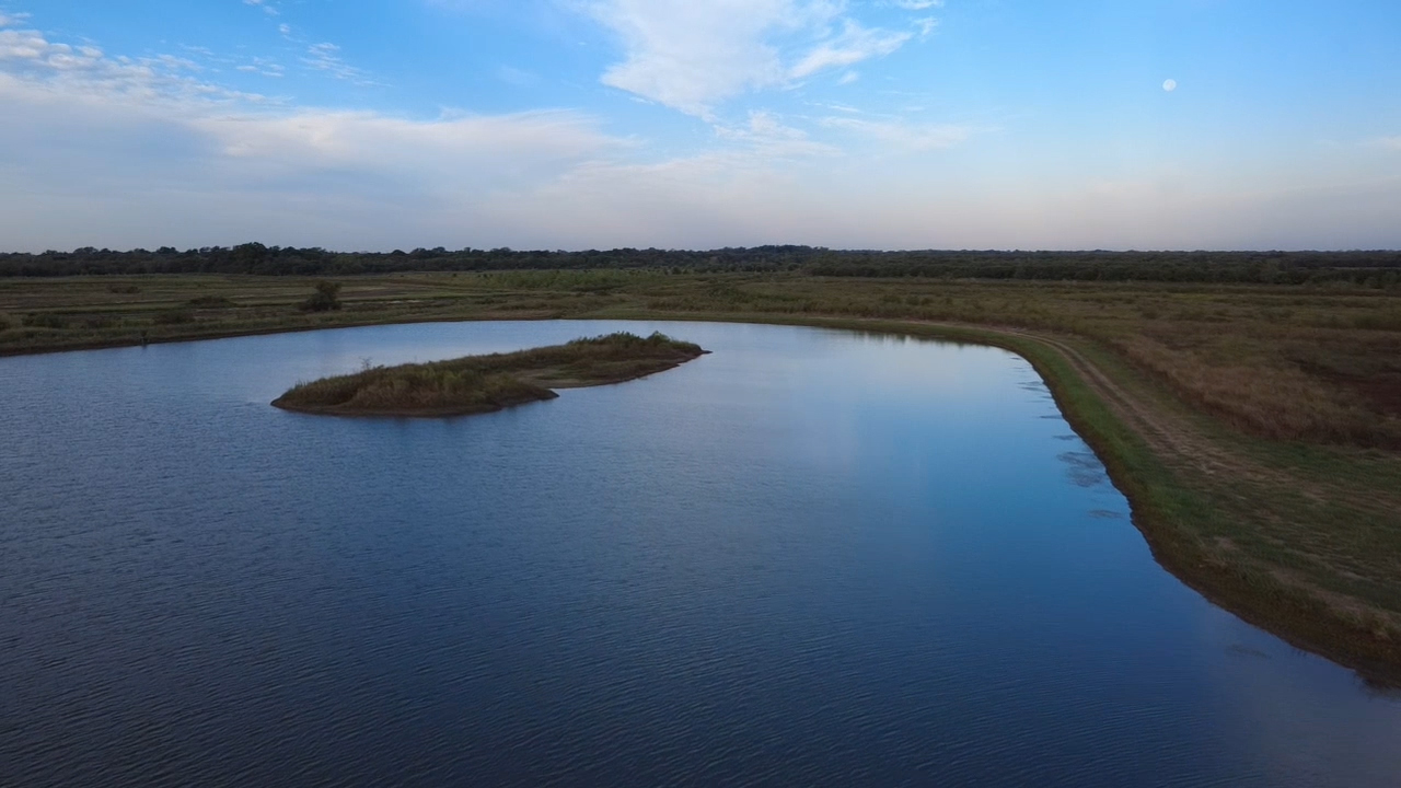 Calm river reflecting open sky and distant grassy landscape